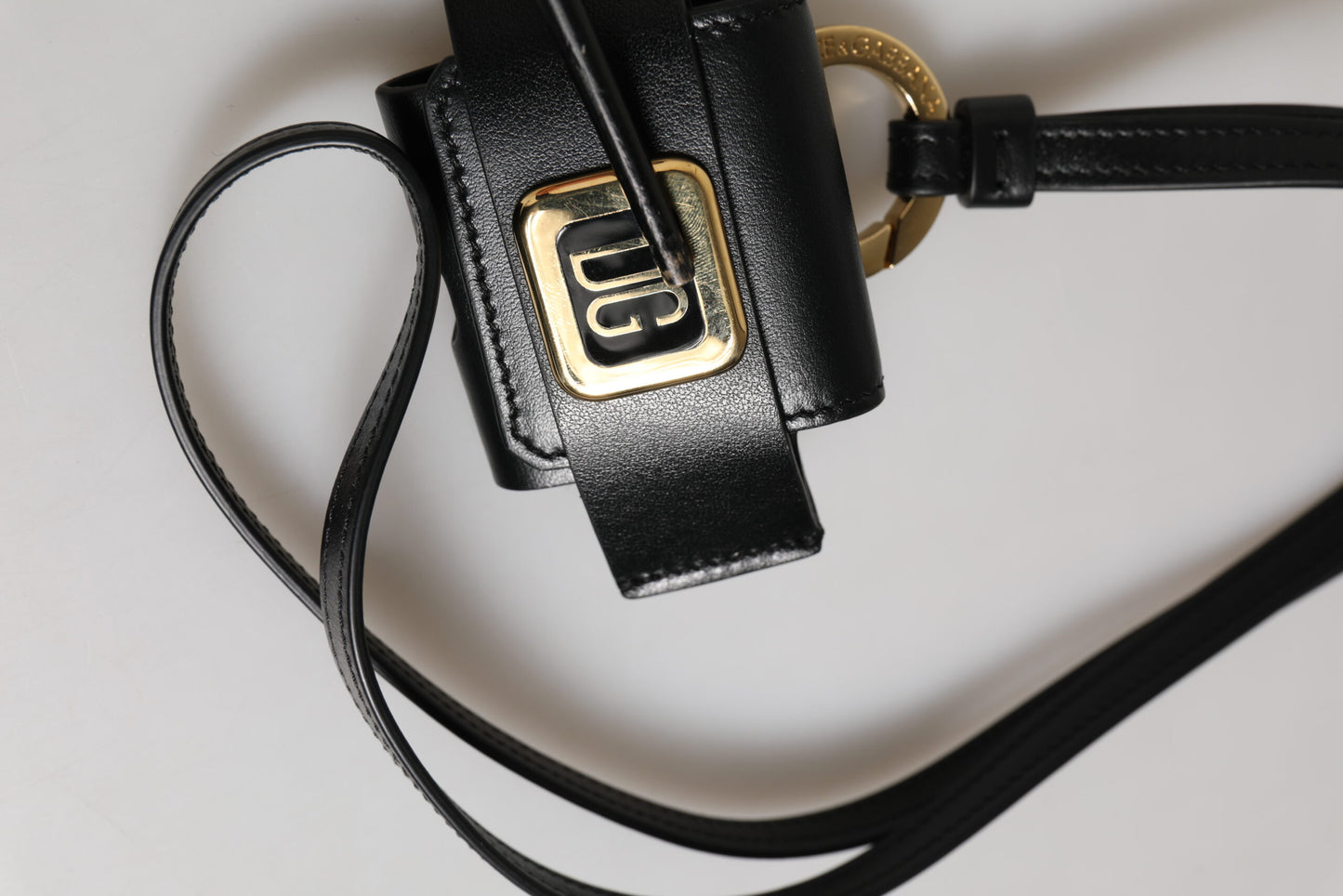 Étui Airpods Dolce & Gabbana en cuir noir avec plaque dorée en métal portant le logo DG.