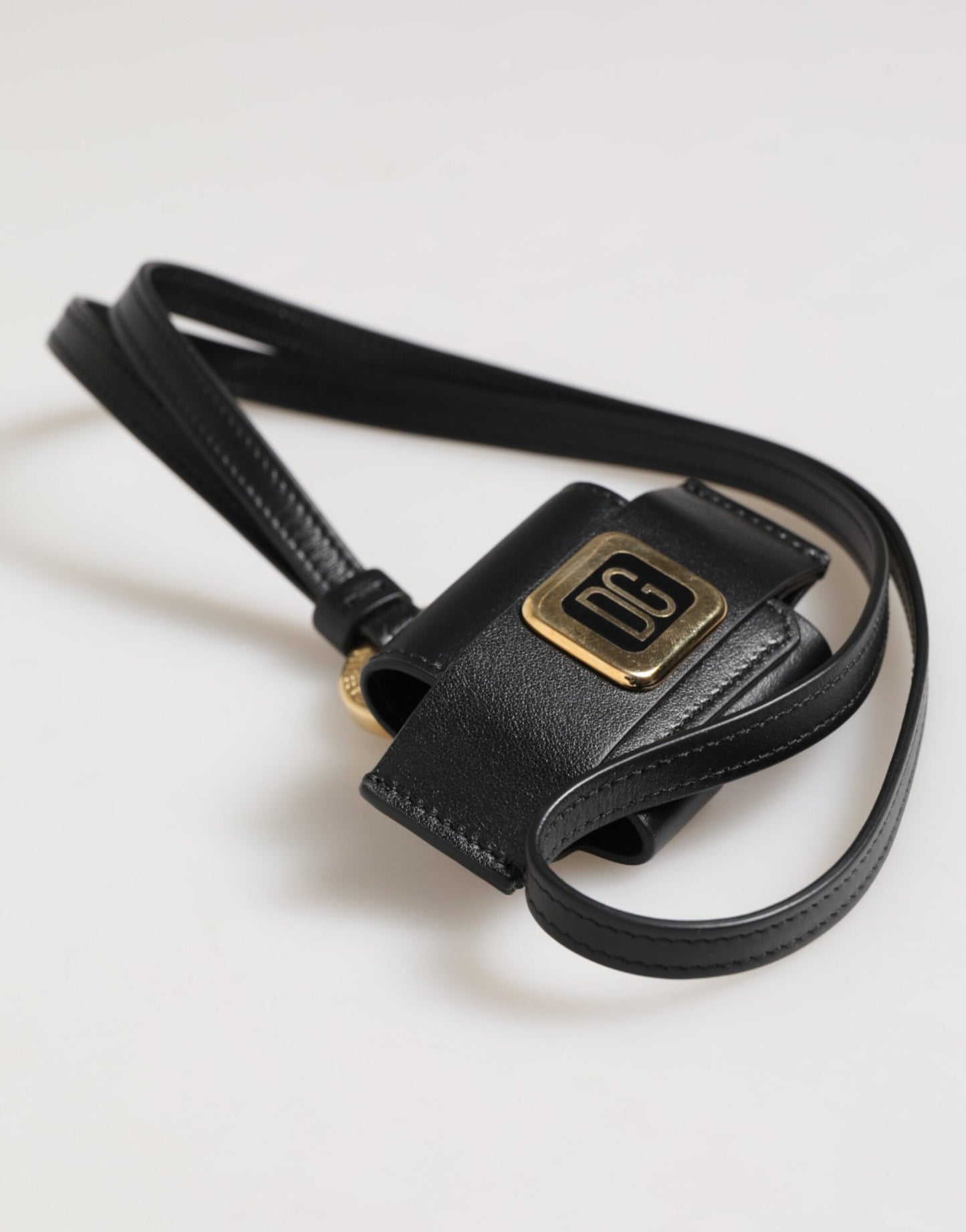 Étui Airpods Dolce & Gabbana en cuir noir avec plaque dorée en métal portant le logo DG.